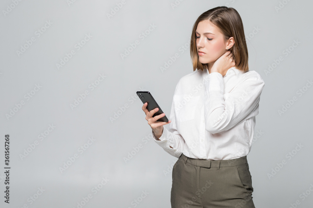 Young businesswoman looking in phone screen holding neck of pain isolated on white background Young businesswoman looking in phone screen holding neck of pain isolated on white background