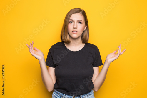 Portrait of young pretty surprised woman with opened mouth standing with open palms on yellow background