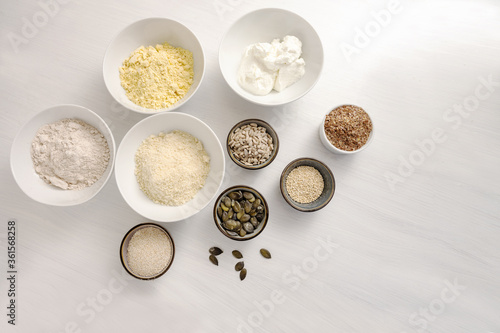 Baking ingredients for a low carb protein bread with quark, oat bran, almond flour and various seeds on a white table, high angle view from above, copy space