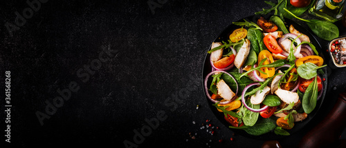 Spring salad with spinach, grilled chicken, cherry tomatoes, arugula, corn salad and red onion. Healthy food concept. Black stone table. Top view. Panoramic banner with place for text