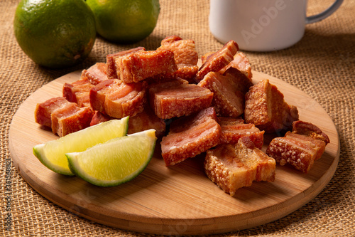Deep fried crispy pork belly served with two half lemon on the table.