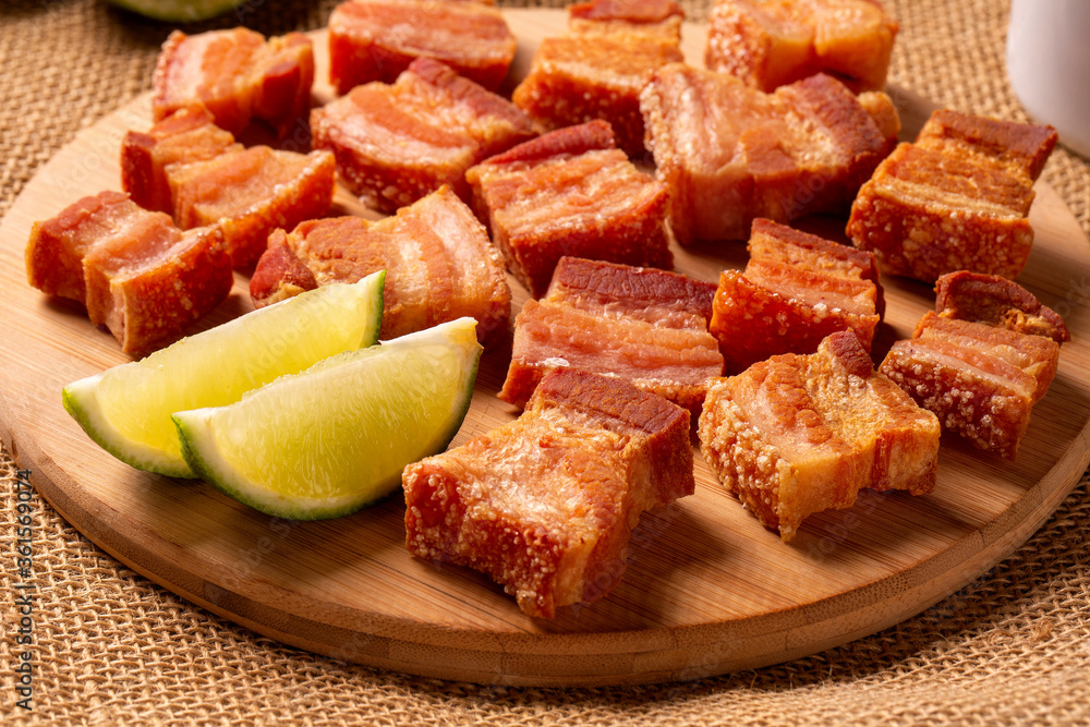 Deep fried crispy pork belly served with two half lemon on the table. Deep fried crispy pork belly served with two half lemon on the table.