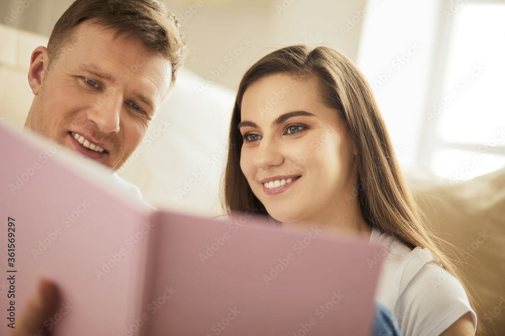 Cute couple unpacking cardboard boxes in their new home, sitting on the floor and looking at a family album Cute couple unpacking cardboard boxes in their new home, sitting on the floor and looking at a family album