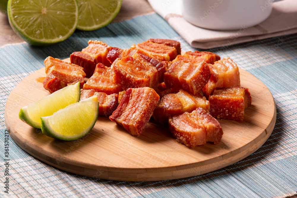 Deep fried crispy pork belly served with two half lemon on the table.