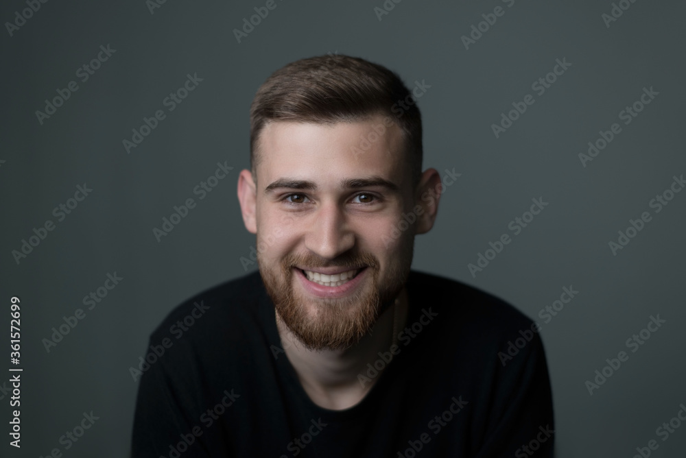 portrait of a young bearded cheerful guy, twenty-five years old, in black. looking at the camera, smiling. Studio photo on a gray background