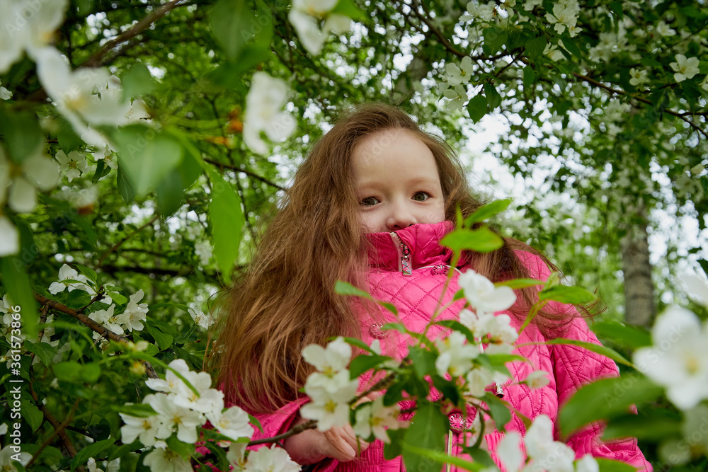 Pretty cute little girl with long hair and in pink glasses posing near a blooming apple tree with white flowers in a summer park Pretty cute little girl with long hair and in pink glasses posing near a blooming apple tree with white flowers in a summer park