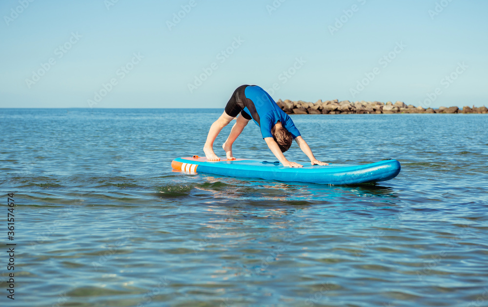 Cute teen child boy having fun and making yoga on sup board in water in Baltic sea