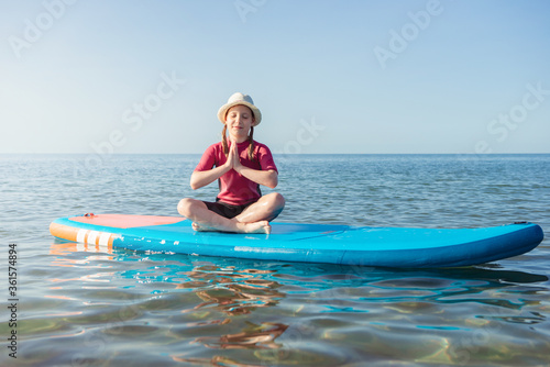 Cute child girl having fun and making yoga on sup board in Baltic sea