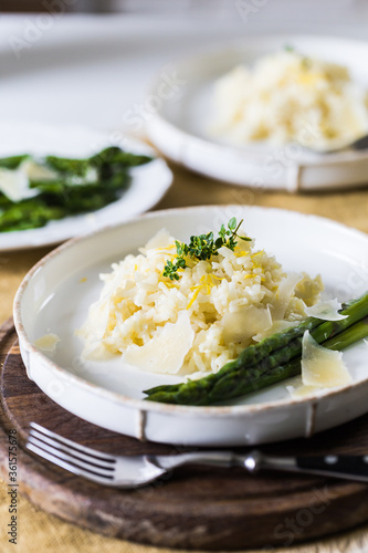 Creamy lemon risotto with parmesan and asparagus on white plate.