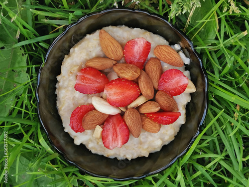 Oatmeal Porridge with Strawberries and muts in bowl on the grass. Healthy Breakfast with Oatmeal and Fresh Organic Berries. photo