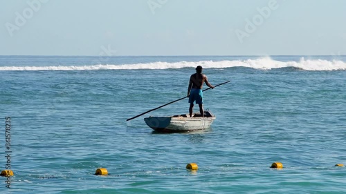 Fisherman on pirogue (boat) on tropical sea with crashing waves - Mauritius