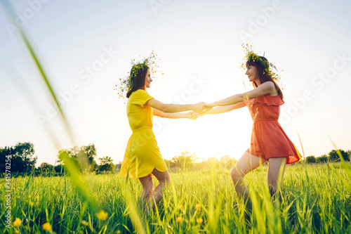 Two young girls in bright dresses are circling in the field. Summer evening in nature