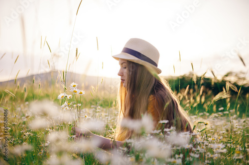 A young girl in a straw hat gathering flowers on the summer field