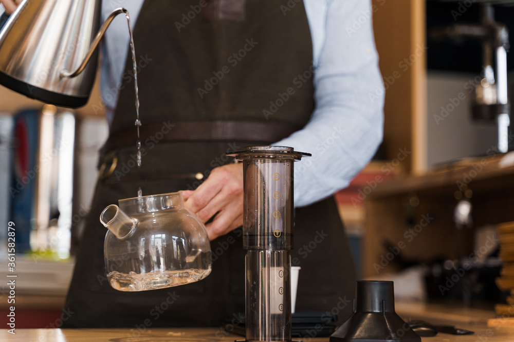 Aeropress coffee alternative making by barista in the cafe. Barista pours hot water in pot for making aeropress coffee with special device. Advert for cafe, restaurants.