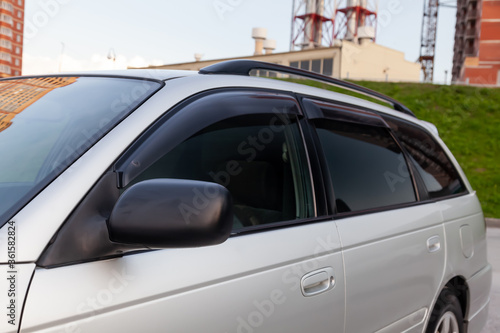 Close-up of the side left mirror and the window of the car body of a gray sedan in a street parking lot after washing and detailing in the field of car service. Pre-sale preparation. © Aleksandr Kondratov