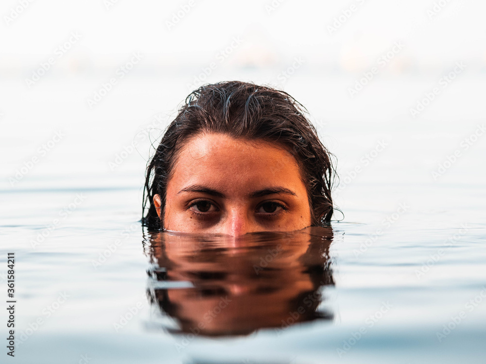 Young caucasian female swimming in the sea with half face submerged underwater