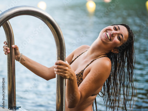 Young caucasian female in a brindle bikini posing in the pool holding the handrail and agreat smile photo