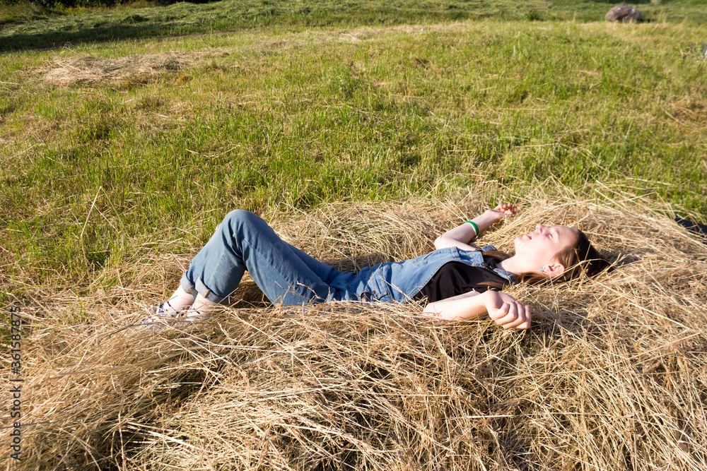 A young woman or teenage girl is lying on the hay, dreaming, resting. Holidays, summer mood, Sunny summer day. A young woman or teenage girl is lying on the hay, dreaming, resting. Holidays, summer mood, Sunny summer day.