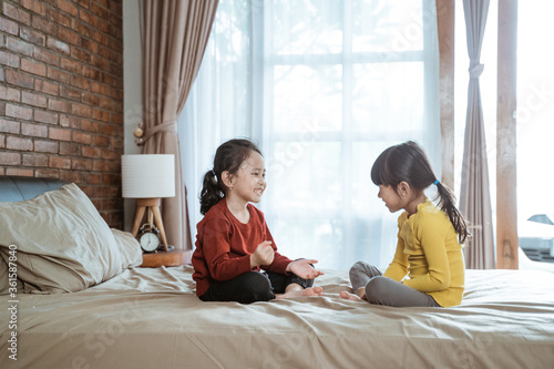 two little girls smiled happily playing together when sitting on the bed in the room
