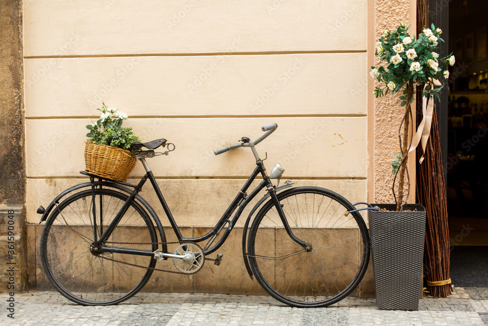 Old Europe style, a bicycle with a basket with fresh flowers is parked near the entrance to the house