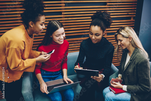 Cheerful multiracial women writing registration documents for training courses sitting together with modern technology, happy female students signing pepers of information agreement before workshop photo