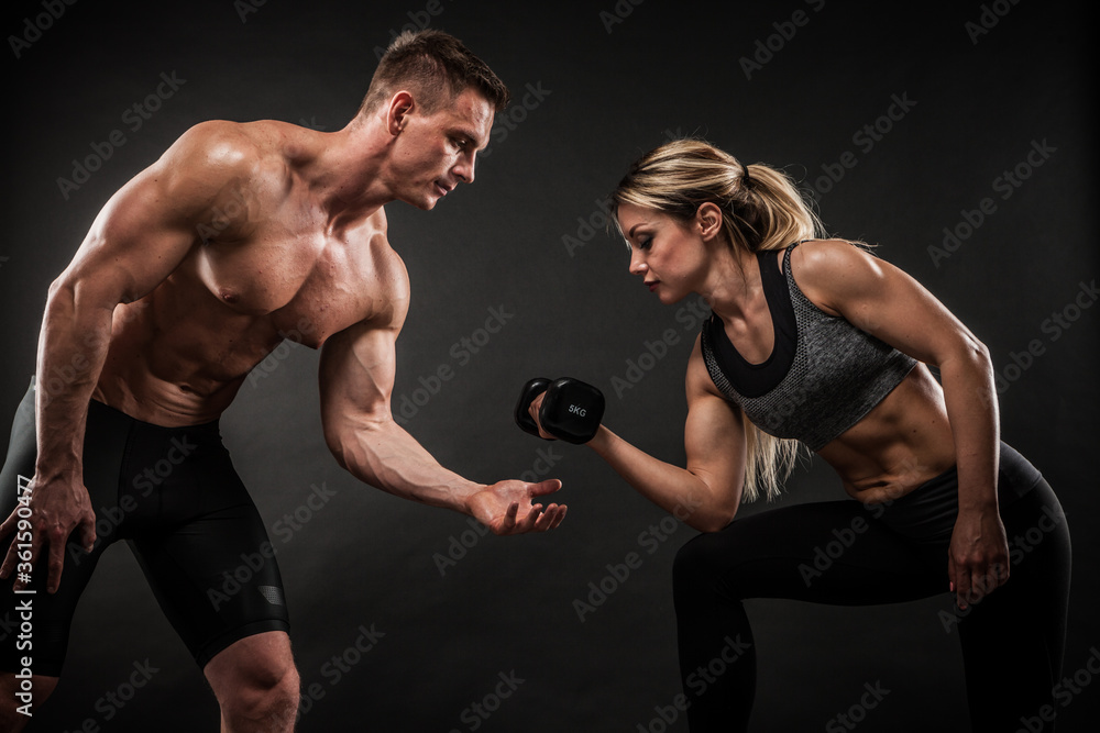 Fitness in gym, sport and healthy lifestyle concept. Couple of athletic man  and woman showing their trained bodies on black background. Two bodybuilder  models standing and demonstrating tight muscles. foto de Stock
