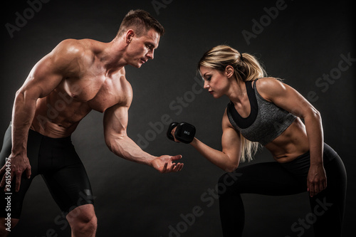 Fitness in gym  sport and healthy lifestyle concept. Couple of athletic man and woman showing their trained bodies on black background. Two bodybuilder models standing and demonstrating tight muscles.