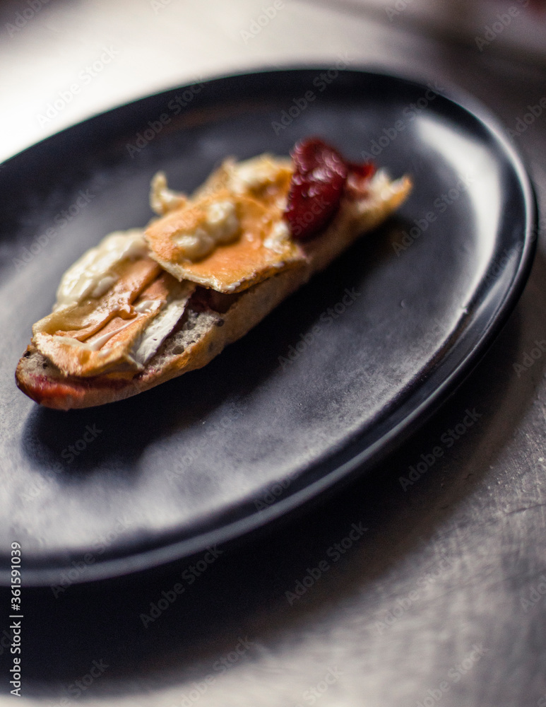 French baguette with hot Camembert cheese with jam in black plate French baguette with hot Camembert cheese with jam in black plate