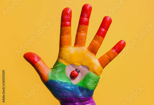 Rainbow colors painted hand with heart shape and a ladybug on it on yellow background