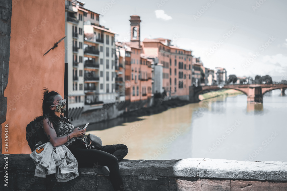 Persona con la mascherina seduta sul ponte vecchio a Firenze, che osserva il telefono. Concetto di viaggio in città ai tempi del covid-19 coronavirus.