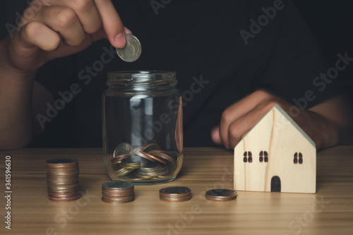 Businessman holding coins putting in glass with house wood model and coin stack front, Business, finance, investment, economics, saving money, saving money, accounting Concept.
