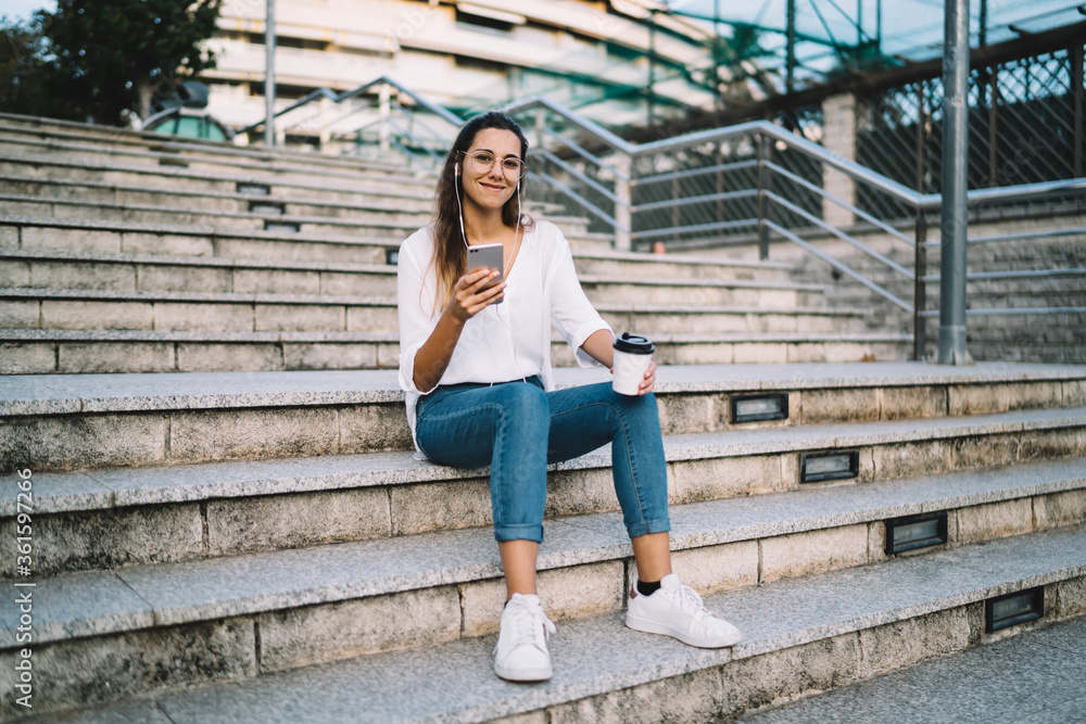 Young woman sitting on stairs with smartphone and cup of coffee
