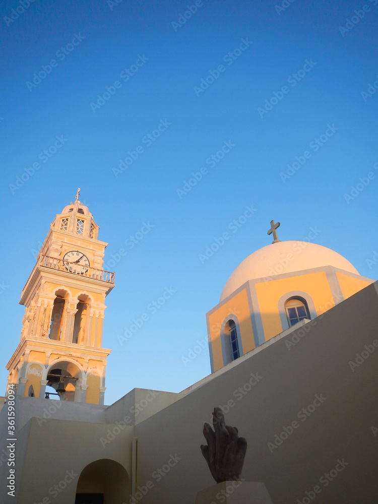 Greek Roman Catholic church. Сhurch dome matching the baroque yellow and gray coloring of the clock tower against sunset clear blue sky.
