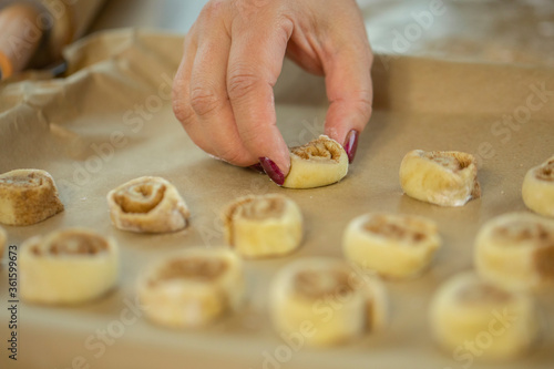 lady's hand lays cinnamon dough rolls on parchment-papered baking tray for preparing gluten-free rolls in kitchen сookery class selective focus family traditions concept Homemade baking lesson concept