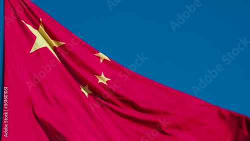 Chinese Flag Wiggles the Wind. The Big State Flag is illuminated by the sun and flutters epically in the wind against the blue sky. Slow Motion 240 fps photo