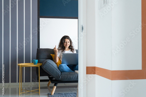 Beautiful girl sitting with a laptop on a sofa in a stylish room. Work from home. Work atmosphere in a good mood