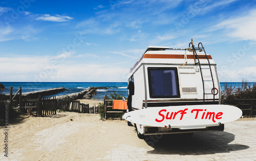 Rear view of vintage camper parked on the beach against a beautiful scenic view - Caravan of surfer with a surfboard on back - Nomadic life concept of surfer waiting for better waves - Surf Time text