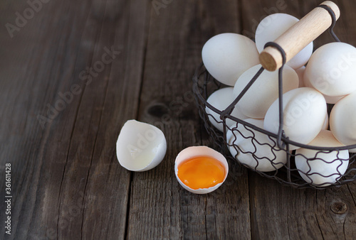 Vintage metal basket of raw eggs next to eggshell with  yolk on rustic wood table