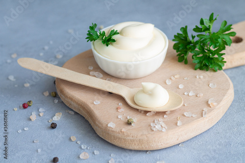 Bowl fresh organic homemade mayonnaise next to wooden spoon with mayo on wood board