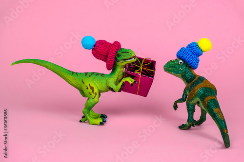 cute green toy dinosaur in knitted hat give present box to another dinosaur in hat, festive funny greeting card © dvulikaia