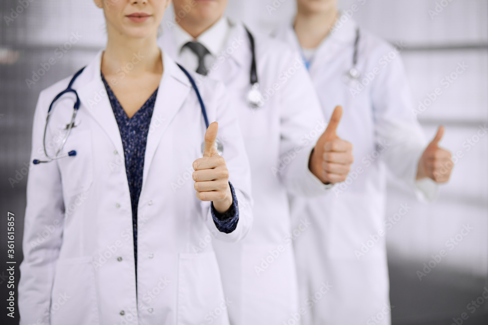Doctors standing as a team with thumbs up in clinic and ready to help patients. Medical help, insurance and medicine concept Doctors standing as a team with thumbs up in clinic and ready to help patients. Medical help, insurance and medicine concept