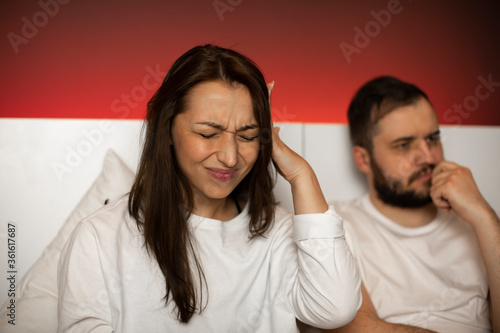 Young married couple in bedroom. Woman with headache holds hand at temple suffers from migraine, upset man thinks about problems in sexual life. Relationship problems in intimate life, illness malaise