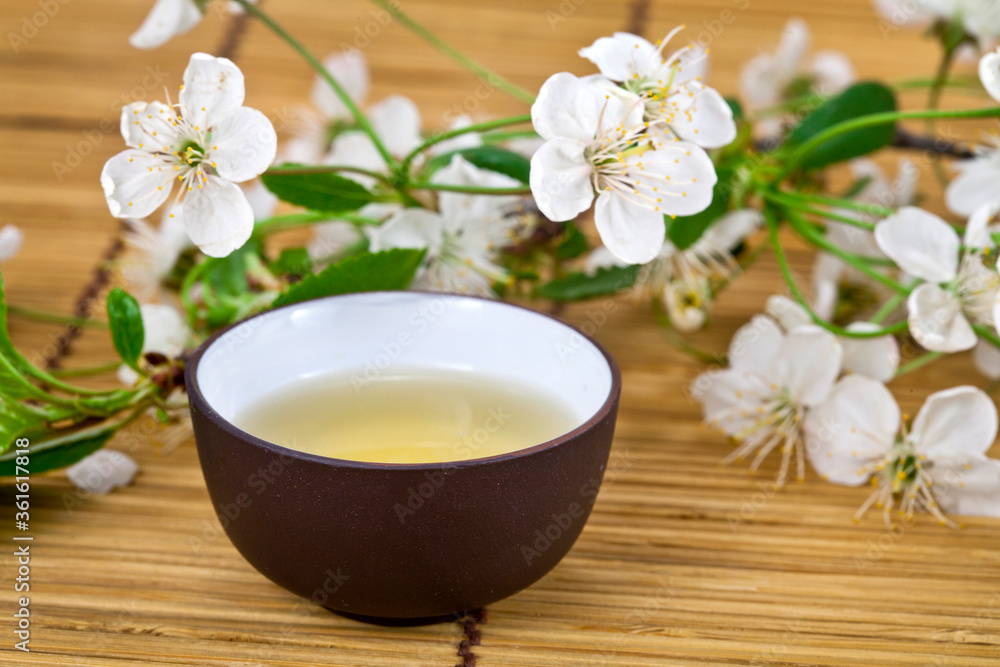 Green tea in a ceramic cup with branches of blossoming cherry tree on a bamboo background. Spring background.