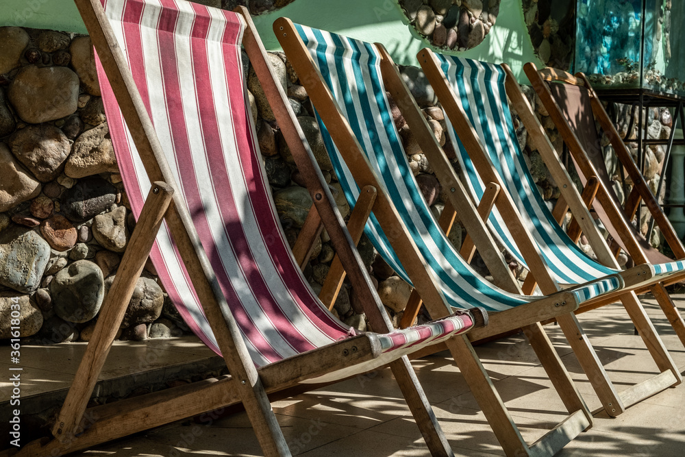 Empty striped sun loungers in the courtyard of the guest house. Fabric, folding chairs for tourists. Day. Summer. Georgia. Resort. Empty striped sun loungers in the courtyard of the guest house. Fabric, folding chairs for tourists. Day. Summer. Georgia. Resort.