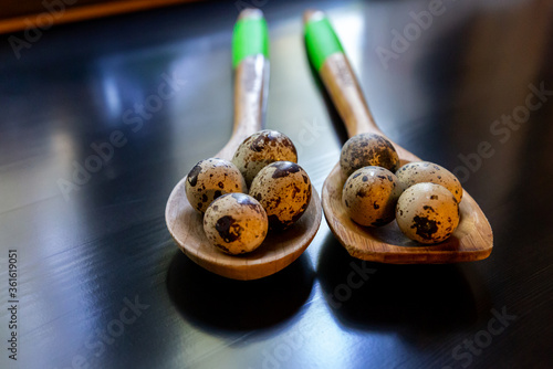 Quail eggs with speckles in two wooden spoons with light green handles on a dark shiny table. Healthy eating, bird eggs. Cooking breakfast, ingredient, cuisine. Group of objects, close-up.