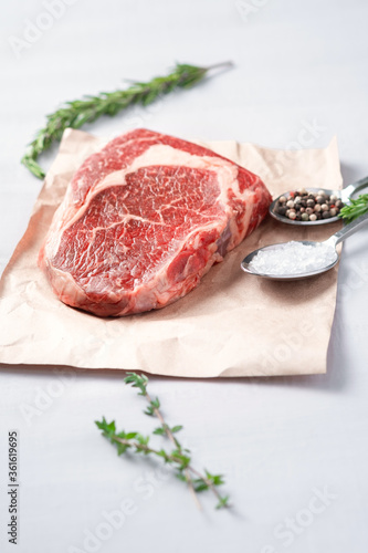 Raw rib eye steak on craft paper with cooking ingredients and spiced spoons