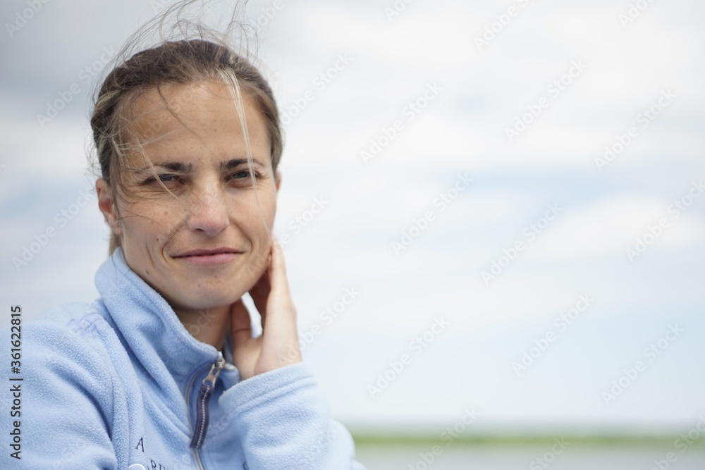 A portrait of a woman in her 20s/ 30s. She is smiling and looking at the camera. In the background, you could see a body of water -lake, river, pond, etc. A portrait of a woman in her 20s/ 30s. She is smiling and looking at the camera. In the background, you could see a body of water -lake, river, pond, etc.