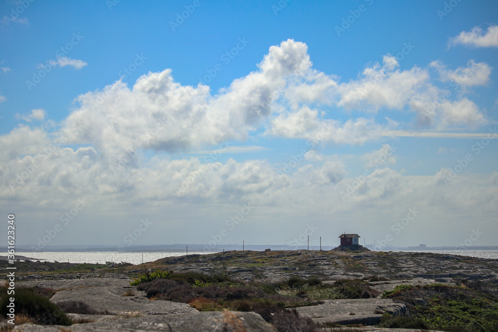 View of a small cabin on a rocky hill.
Shot in the coastal region of western Sweden. The small cabin is isolated in a rugged landscape, with blue sky and fairly dramatic clouds