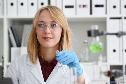 Smiling beautiful technician woman portrait and sample bottle with poison fluid. Medical worker in uniform use reagent tube for virus infection exam or biological toxic reaction  drug creation