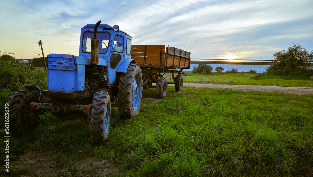 blue tractor with a trailer in a field on a summer evening blue tractor with a trailer in a field on a summer evening